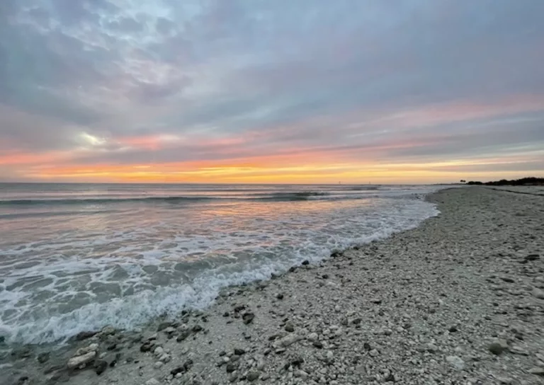 Sunset in Tampa with beautiful sky filled with pinks, oranges, and yellows, and the ocean and sandy beach.