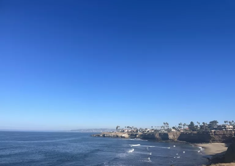 View of Ocean Beach San Diego from OB Pier featuring blue ocean and blue sky and city in the background.