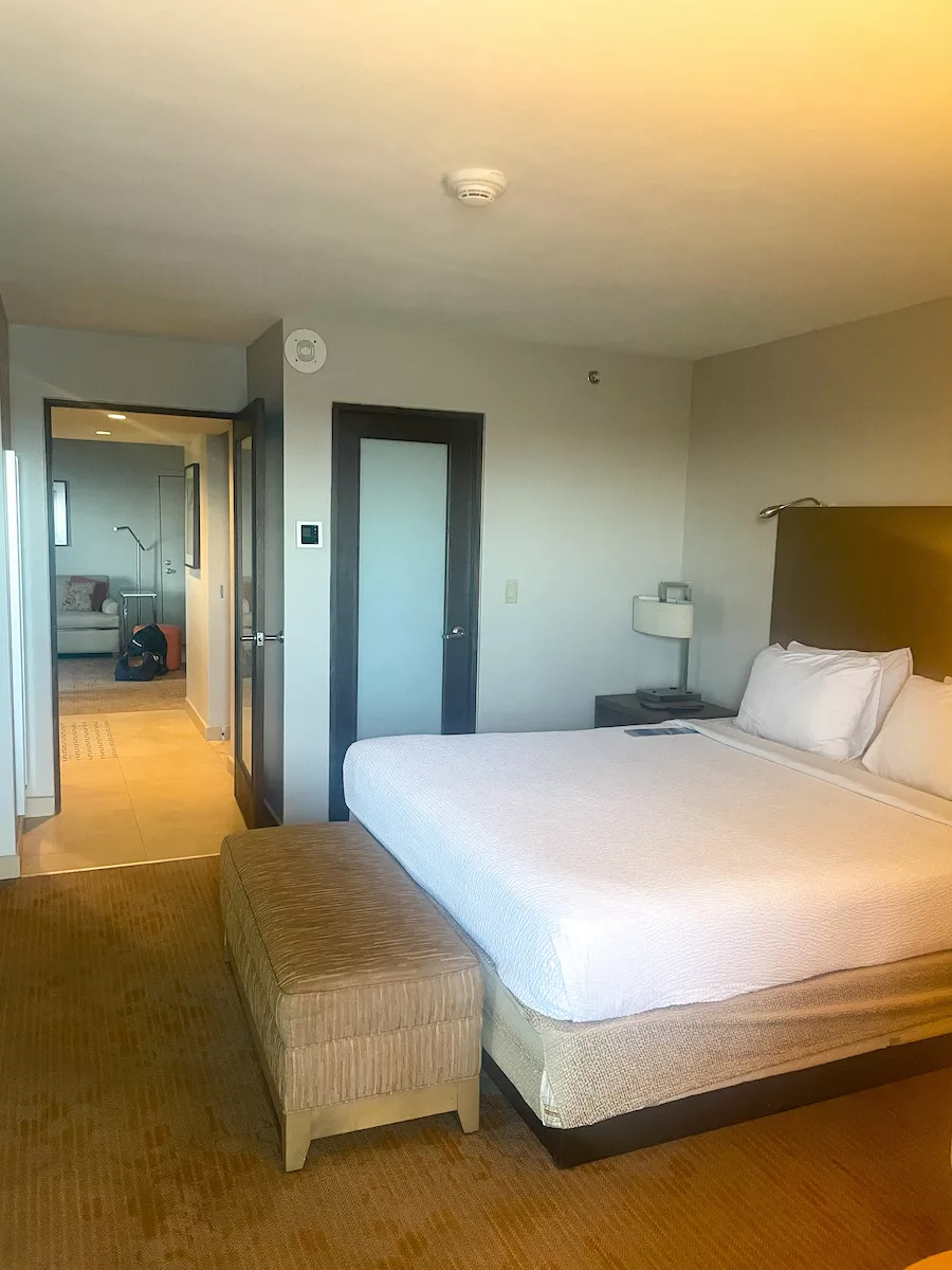 View of bedroom, including bed and looking into the living room at the Courtyard Isla Verde Beach Resort in San Juan, Puerto Rico. 