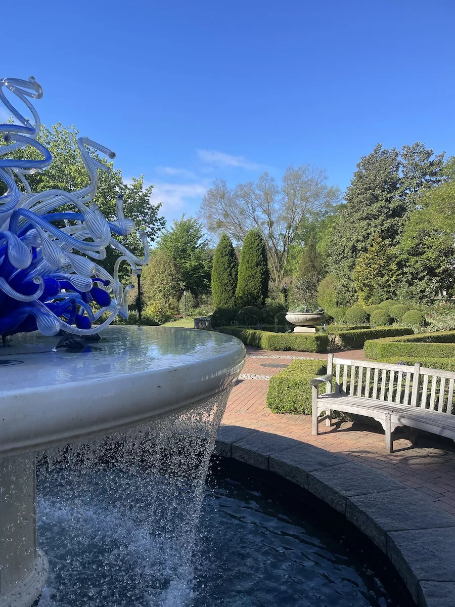 View of fountain, bench and gardens. 