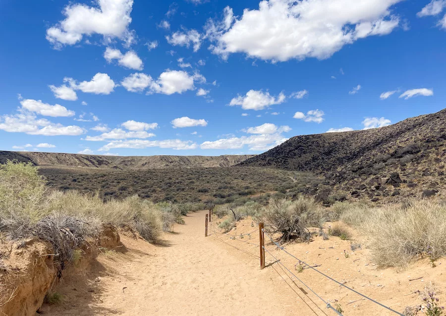 View from a trail in Petroglyph National Monument of blue, cloudy sky and mountains in the distance. 