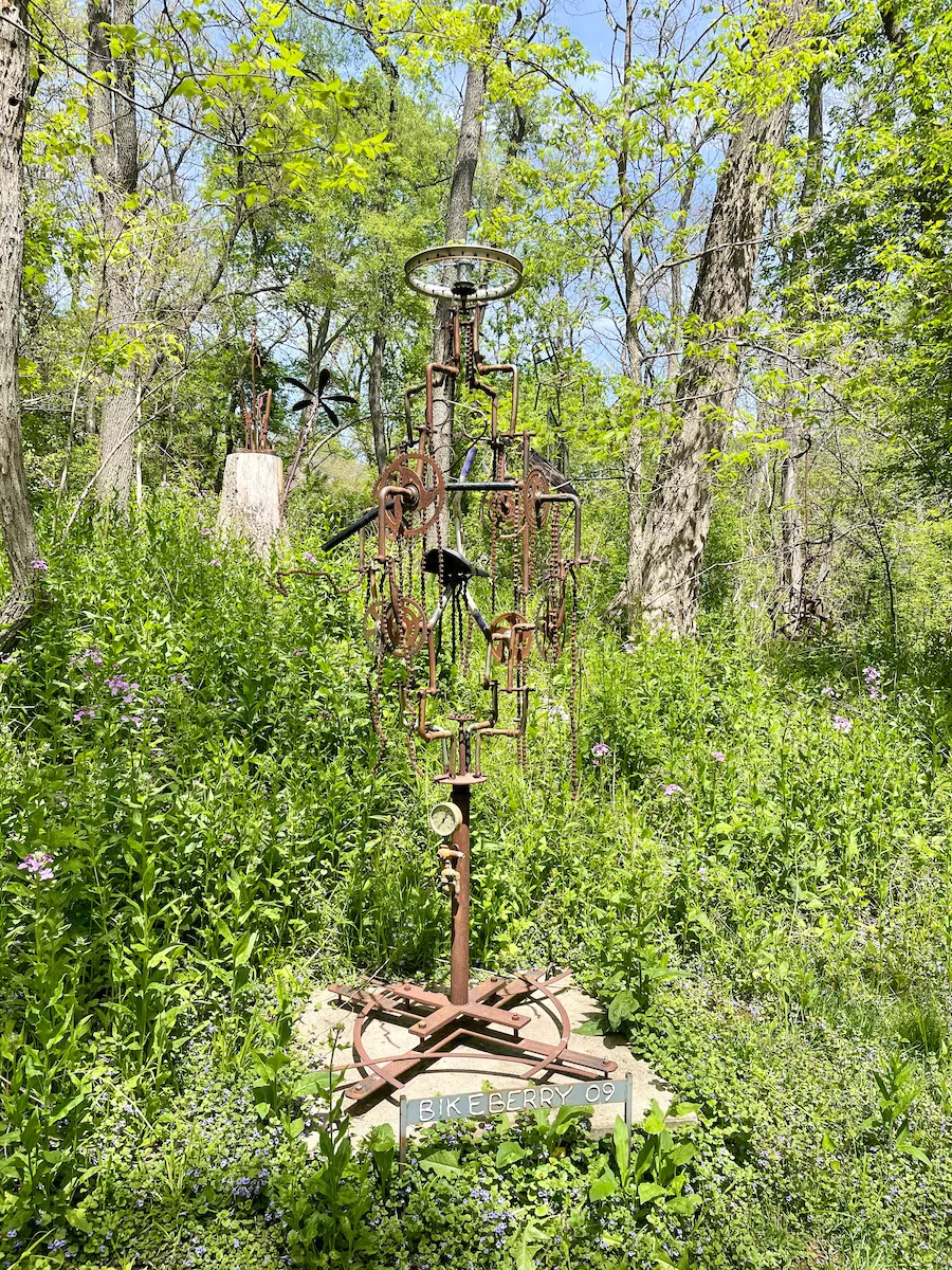 Tall steel sculpture of bicycles in a yard surrounded by grass. 