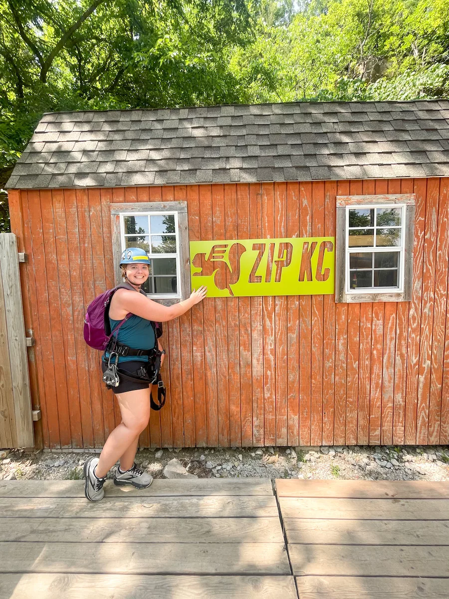 Woman in ziplining harness and helmet standing in front of ZIP KC sign in Kansas City