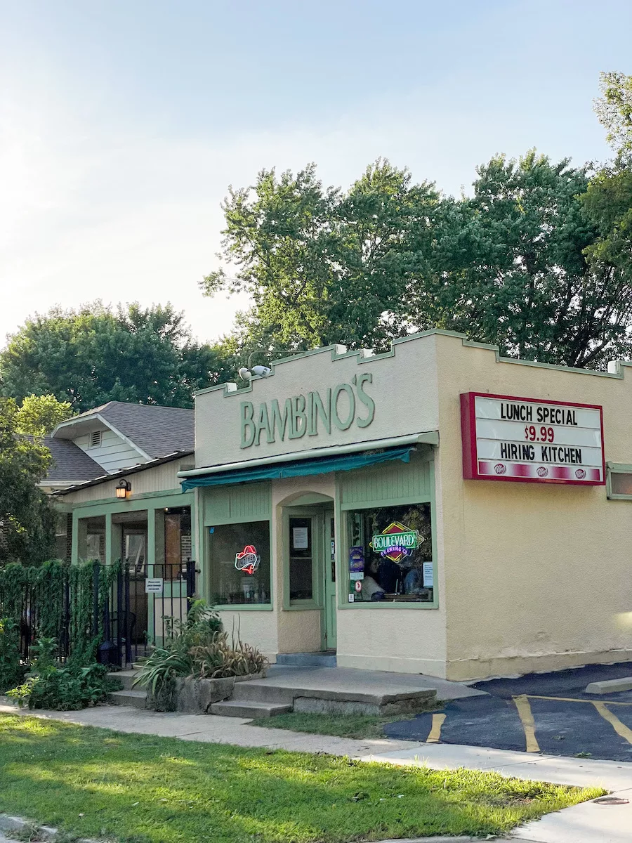 Outside view of Bambino's Cafe in Springfield, MO, including the outdoor seating area. Trees and cloudy sky in view behind the building. 