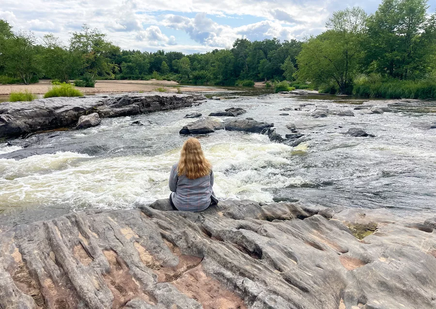 Outdoor Activities in Eau Claire - rocks, water and beach areas surround by trees and a cloudy blue sky. 