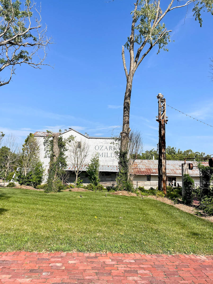 Restaurants in Springfield - View of Ozark Mill at Finley Farms from the parking lot. Old historic building surround by trees and a paved walkway. 