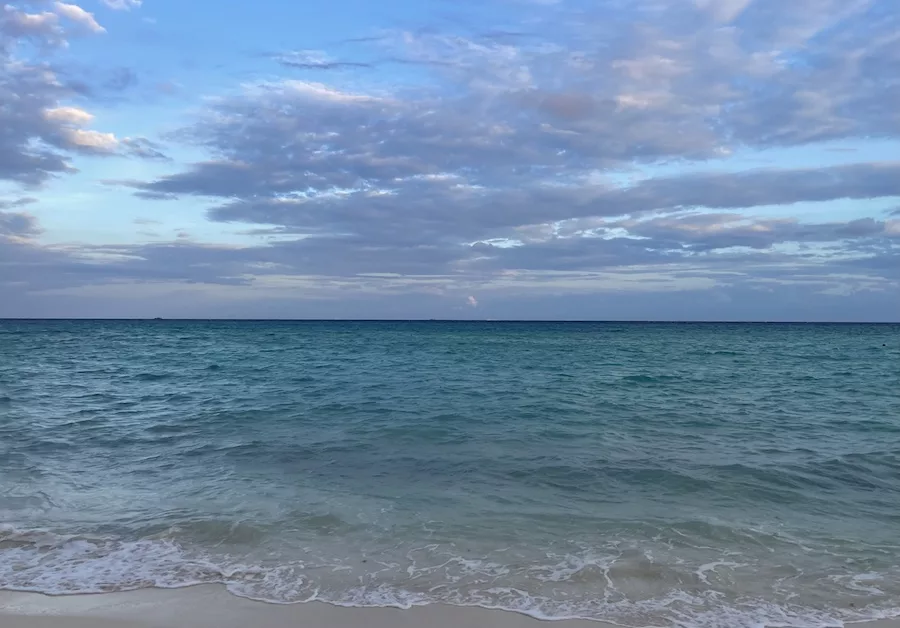 View of turquoise blue ocean from a beach in Cancun, Mexico surrounded by a light and cloudy sky. 