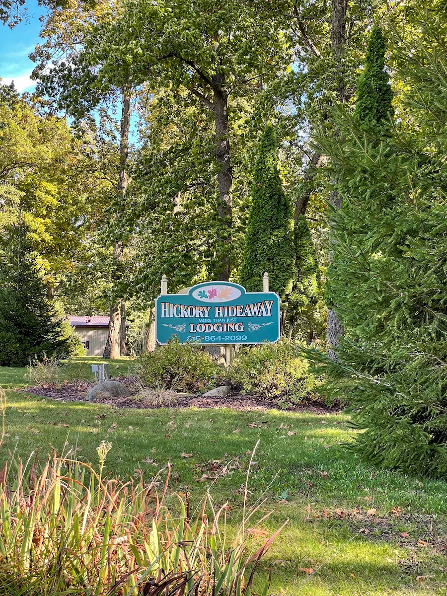 Entrance sign to Hickory Hideaway cabins surrounded by green grass, trees, and brush in Carroll County.