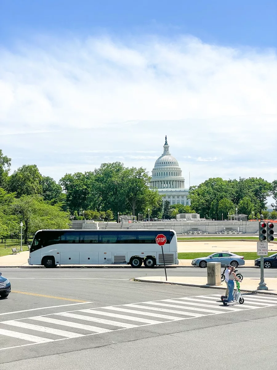 Image of Capitol in Washington DC from afar with tourist bus in front and people walking in street 