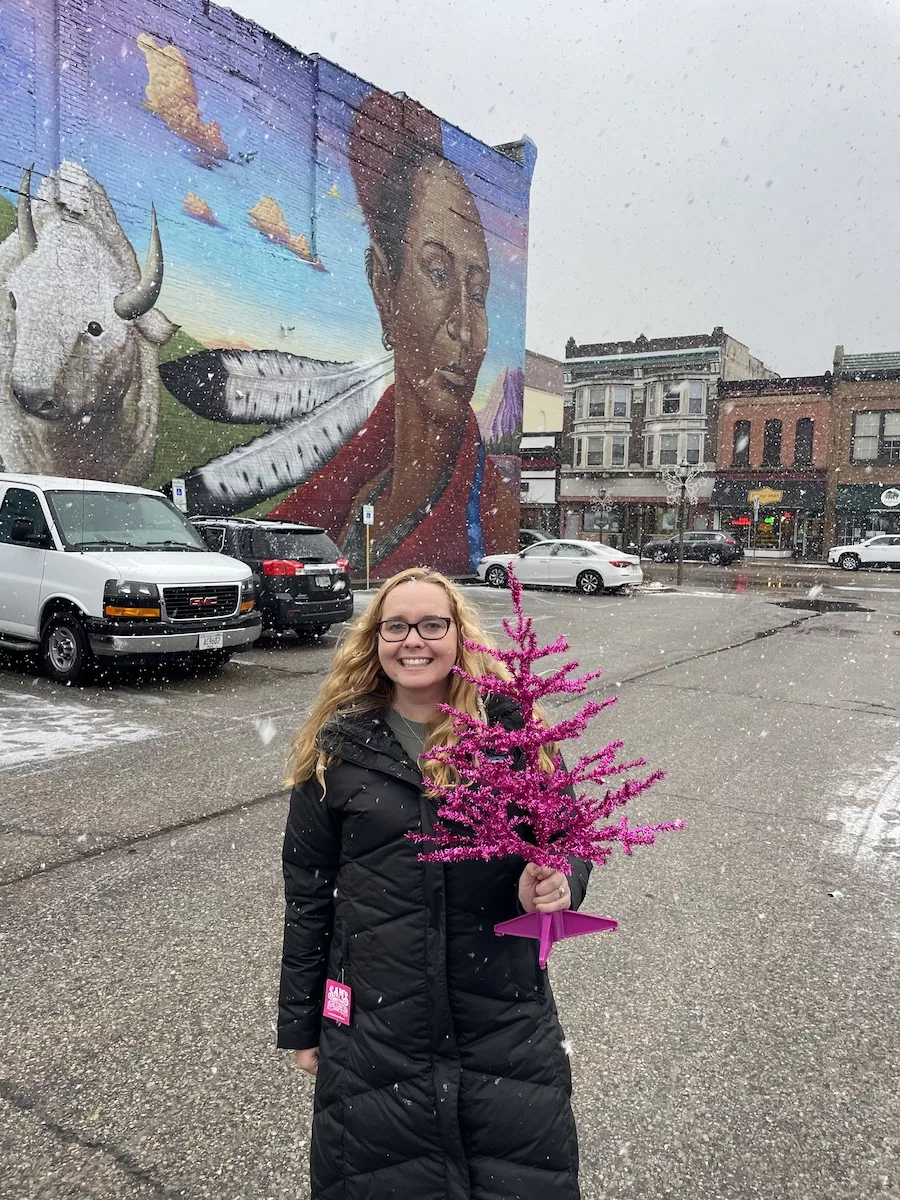 Woman carrying hot pink christmas tree next to beautiful mural of woman. 