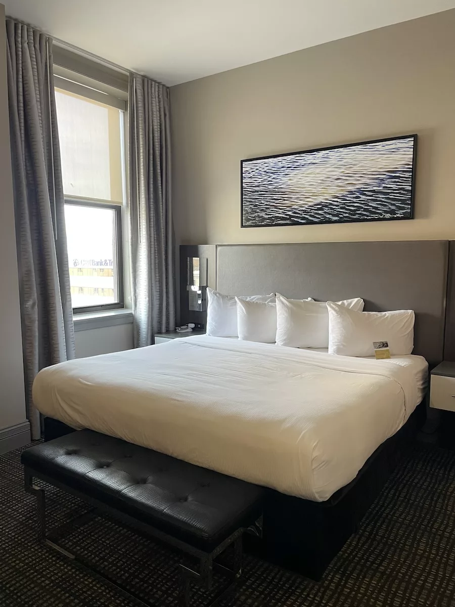 View of a bed with an open window and painting above bed at the Hotel Current Iowa in Downtown Davenport 