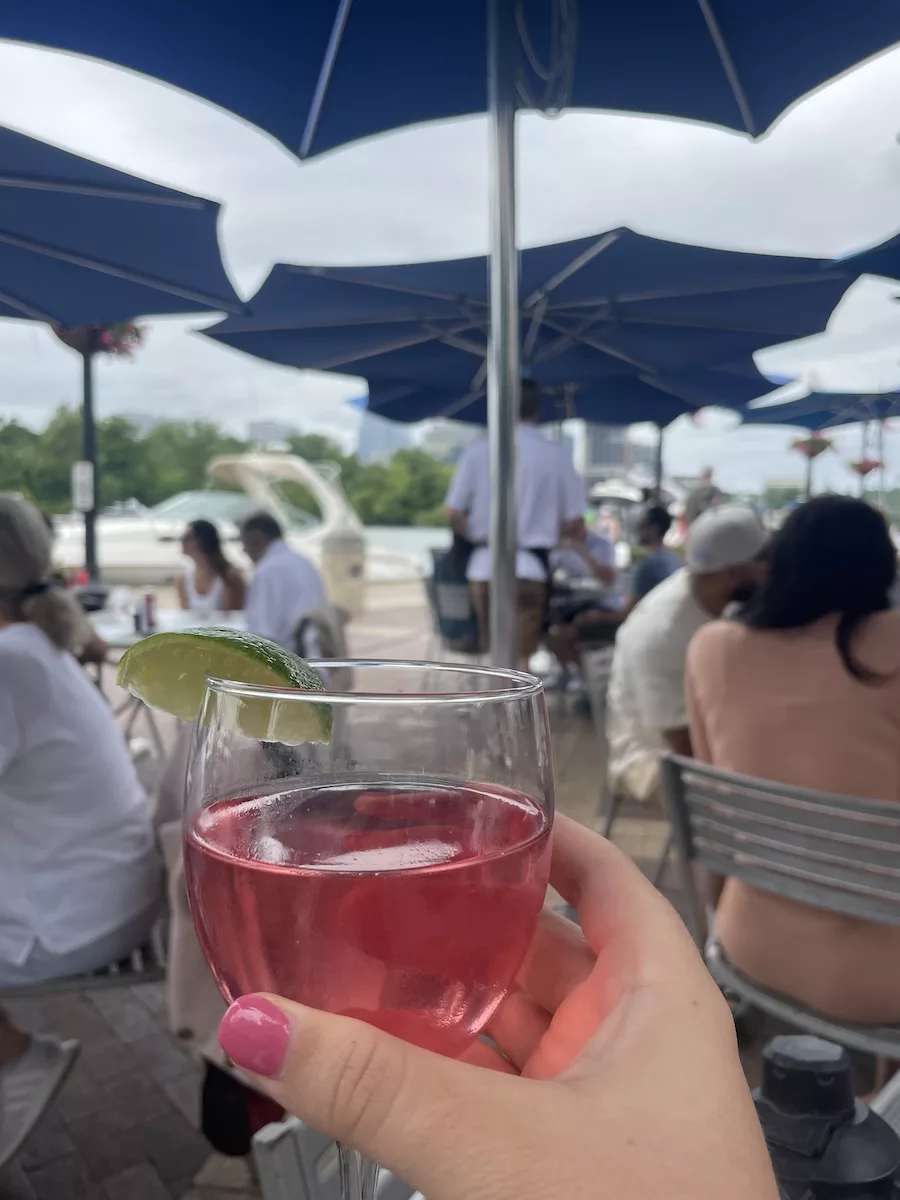 Image of lady with painted nails holding a half-filled wine glass while dining outside. 