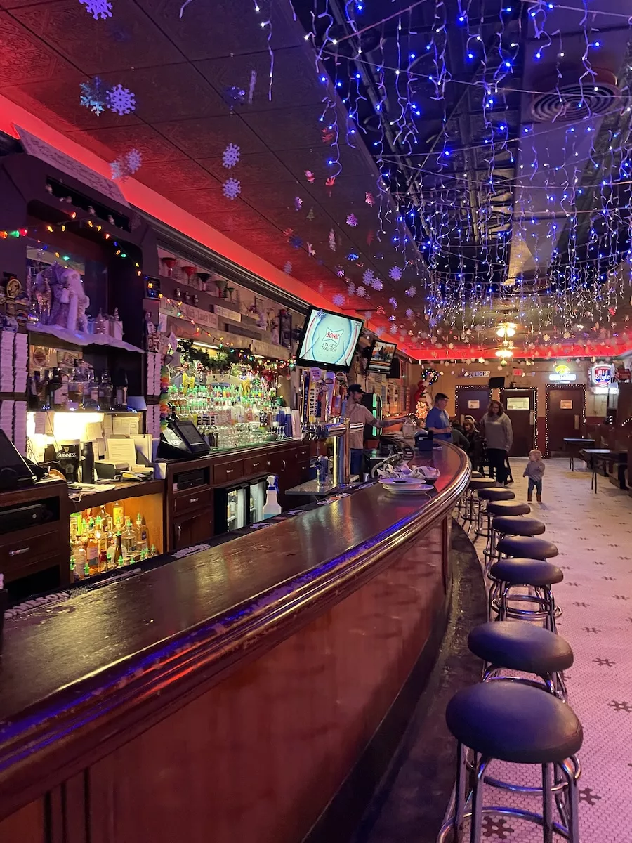 Image of large wooden bar and bar stools with tables in the background 