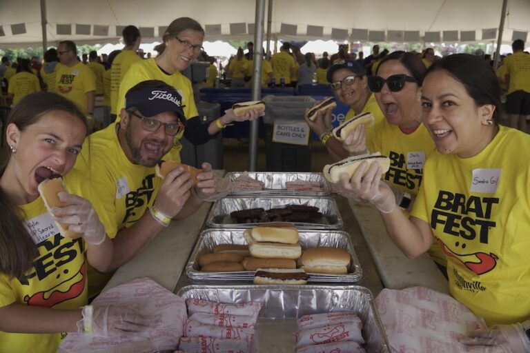 Volunteers in yellow brat fest shirts eating brats under a tent - Madison, WI