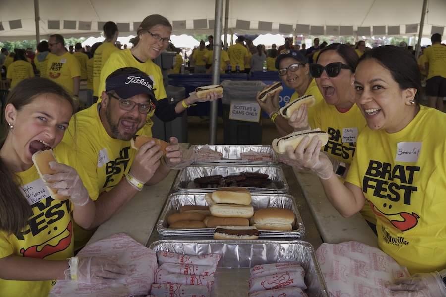 Volunteers in yellow brat fest shirts eating brats under a tent - Madison, WI