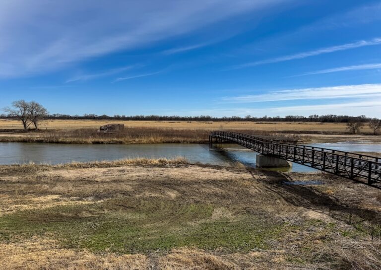 View of bridge, grass, and Platte River with a deep blue sky in Grand Island Nebraska at the Crane Trust Nature Center.