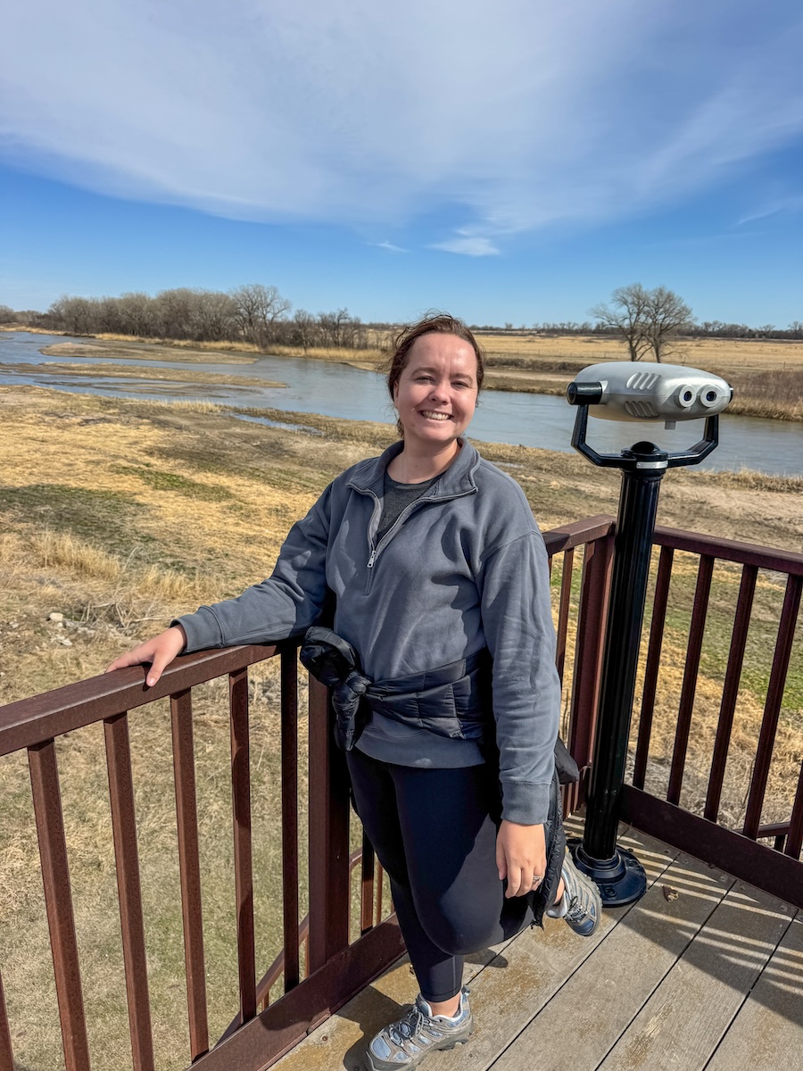 Image of young woman posing on an observation deck overlooking a plains area with a cloudy blue sky in Grand Island, Nebraska.